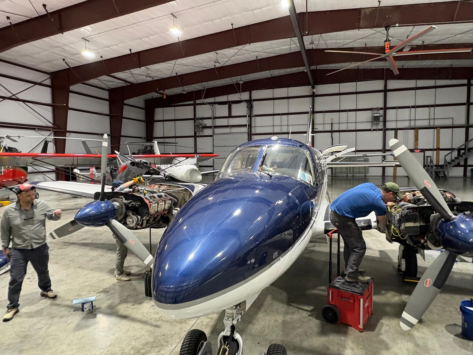 Twin piston aircraft receiving maintenance inside a hangar.