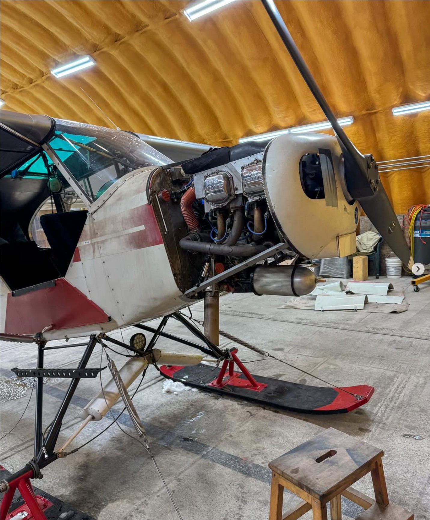 Super Cub aircraft on skis with engine cowling open inside a hangar.